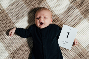 Baby's first month milestone celebration. A one-month-old baby lies on a textured blanket, holding...