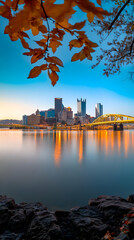 Cityscape Reflects in Calm River at Dawn with Autumn Leaves Framing the Scene Peacefully
