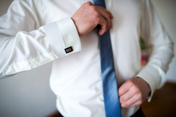 Preparing for a formal event with style. A man adjusts his tie and shirt cuffs, getting ready for a formal occasion in a well-lit indoor setting.