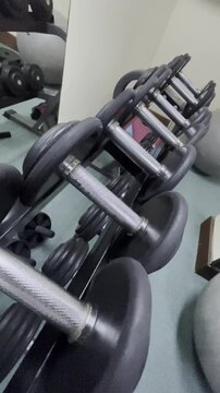 A row of black dumbbells on a gray metal stand. Exercise and fitness gym equipment for strength and weight training. Workout and athletic equipment.