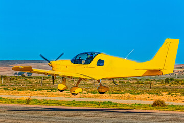 Bright yellow two-seater low-wing light-sport aircraft taking off from a small airfield in the Western Cape, South Africa