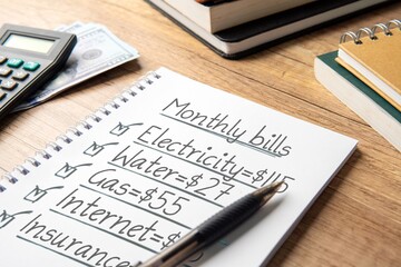 A close-up image of a notebook with a handwritten monthly bills list. Household budget planning and...