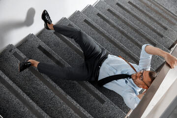 Injured man on stairs in building after fall, above view. Dangerous accident