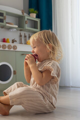 Young child enjoys a toy apple in a bright playroom with a miniature kitchen setup during daylight hours