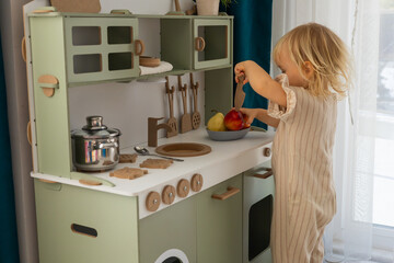 cute toddler blonde baby girl playing on toy kitchen at home,