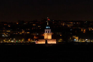 Obraz premium Historic Maiden's Tower glowing at night in Istanbul, Turkey, with the cityscape and Bosphorus in the background. A blend of cultural heritage and modern maritime activity captured in a serene moment.