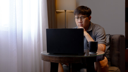 Man wearing glasses and gray collared shirt Focus Working on Laptop in Comfortable Room. Work from home concept