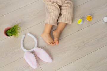 Child lying on the floor with bunny ears and colorful eggs during a playful holiday celebration
