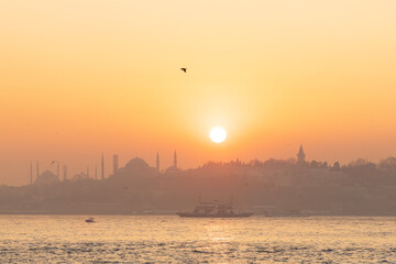 High resolution panoramic photograph capturing Istanbul's historic peninsula bathed in a crimson sunset glow. The city's iconic skyline silhouettes against the vibrant evening sky