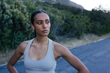 Fototapeta premium Young and confident woman athlete standing on abandoned road and looking away, taking a break during outdoor workout