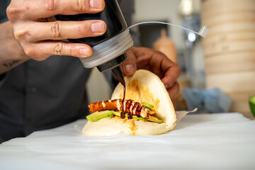 Chef skillfully preparing bao sandwich with avocado, chicken, and sauce in a professional kitchen