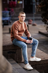 Obraz premium Young man sitting on steps with coffee cup in casual attire