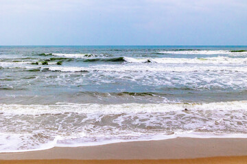 Tranquil beach scene with waves crashing on shoreline under clear sky