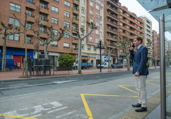 Fototapeta premium Businessman is waiting for the bus and talking on his phone 