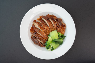 Roast duck with kale, Bok Choy (Chinese mustard greens) in a white plate on a black table, top view