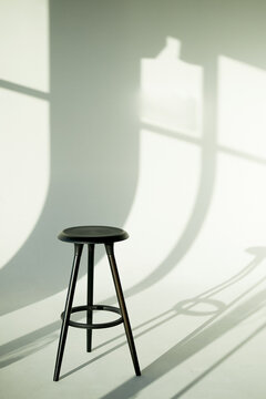 A black tall stool on three legs in a white studio bathed in light. Artist's studio, minimalism