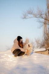 A girl walks with her beloved pet Samoyed in winter on the shore of a lake in the park.