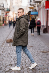 Young Man in Oversized Jacket Walking on Cobblestone Street