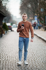 Young Man Walking on Cobblestone Street with Coffee in Hand