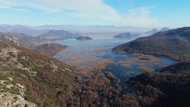 Drone pullback on the Shkodra Lake with its forested cliffs around it under blue sky with clouds