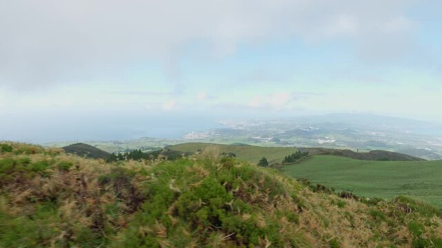 green grassy hillside under cloudy sky with vast fields in the background at the Sao Miguel island