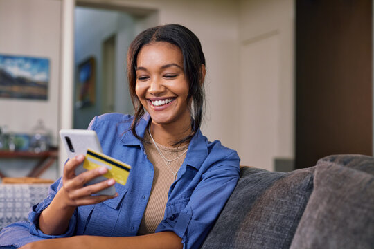 Indian woman making payment through credit card on mobile phone at home
