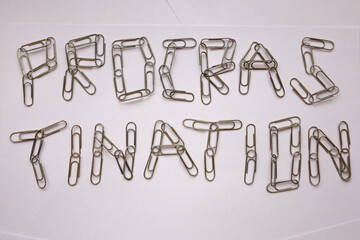 The word "Procrastination", made of metal paper clips on white sheets of paper