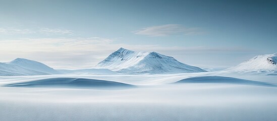 Serene winter landscape with soft snow-covered hills in foreground and majestic blue mountains in background under a clear sky providing ample copy space.