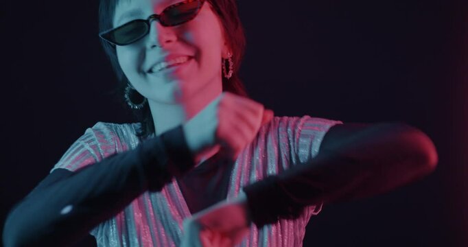 Slow motion portrait of happy Asian woman dancing looking at camera in neon light on dark background. People and modern lifestyle concept.