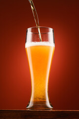pouring beer into glass, wooden stand, red background, close-up view of object, beer foams and bubbles