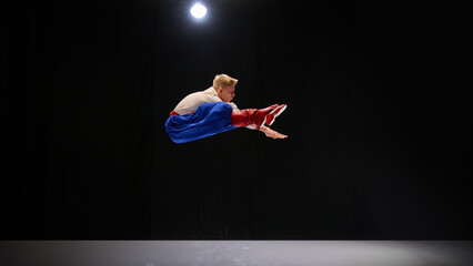 Performer in mid-air leap, dressed in blue trousers and embroidered shirt, arms extended in energetic motion, radiating joy and cultural pride. Concept of traditions, folk style, art and history. Ad
