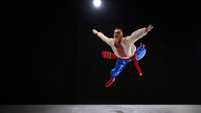 Folk dancer in richly detailed Ukrainian attire, captured mid-spin with broad smile, portraying the spirited storytelling within Hopak against dark background. Concept of traditions, art and history.