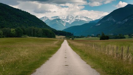Tranquil gravel path surrounded by green fields leading into majestic mountains under a partly cloudy sky with a serene atmosphere.