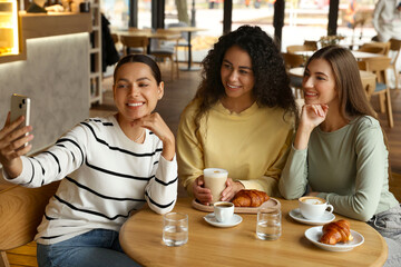 Happy friends taking selfie during coffee meeting in cafe