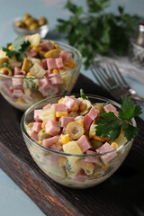 Salad with ham, olives, corn and pineapples in transparent salad bowls on wooden board