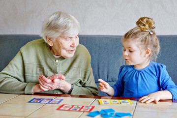 Beautiful toddler girl and grand grandmother playing together pictures lotto table cards game at home. Cute child and senior woman having fun together. Happy family indoors