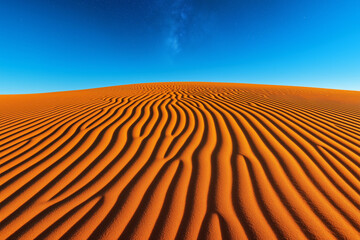 Naklejka premium Rippled sand dunes in a desert glowing under a vibrant blue sky with faint stars at dusk