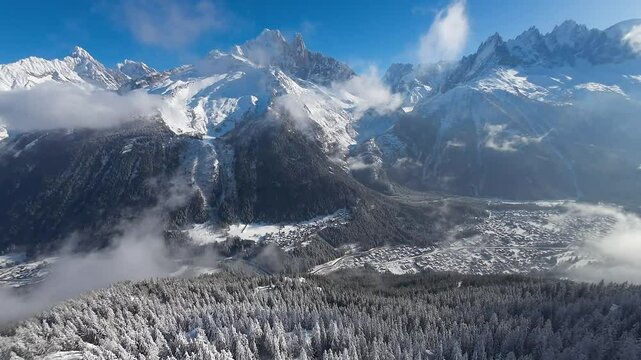 Aerial drone view of Chamonix&rsquo;s ski slopes, surrounded by the towering white peaks of the Alps, offering a stunning winter wonderland with white forests and the town under a bright midday 