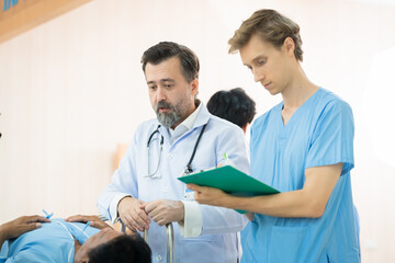 Obraz premium Busy medical care hospital services in waiting area, nurse man in uniform and health care physician female take care of senior patient sitting wheelchair, doctor visits in lobby with group of doctors