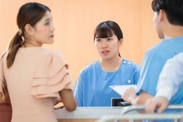 Healthcare professional at reception provides friendly assistance to patient completing registration, doctor trainee male in uniform, reception female services patients, nurse consult with customer.