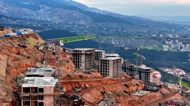 The video shows a multi-story residential construction site. Buildings are at different stages; some in the rough construction phase. The site includes roads, material areas,situated on a hillside.
