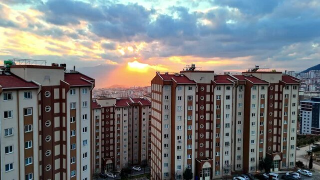 The video shows a wide cityscape at sunset with completed multi-story residential buildings in the foreground. The housing appears to be part of a large-scale residential construction project.