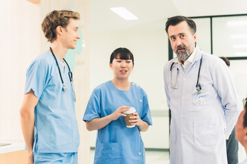 Senior doctor in white coat leads discussion with team of nurses and healthcare professionals, holding tablet in collaborative hospital setting, engages in focused discussion about patient care.