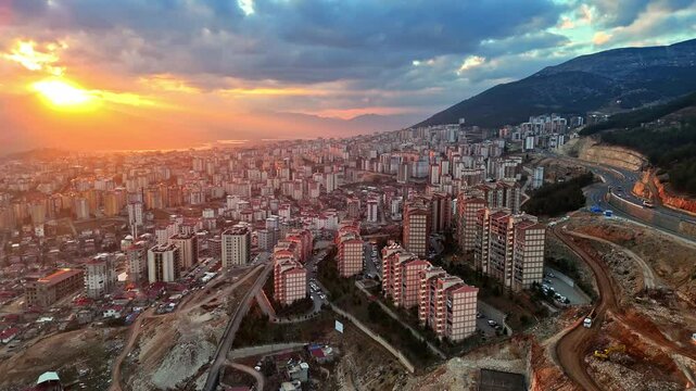 The video shows a wide cityscape at sunset with completed multi-story residential buildings in the foreground. The housing appears to be part of a large-scale residential construction project.