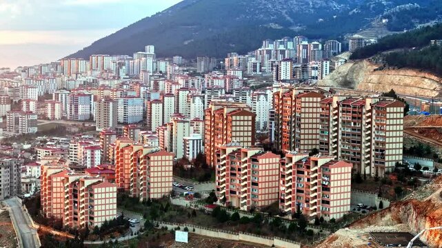 The video shows a wide cityscape at sunset with completed multi-story residential buildings in the foreground. The housing appears to be part of a large-scale residential construction project.