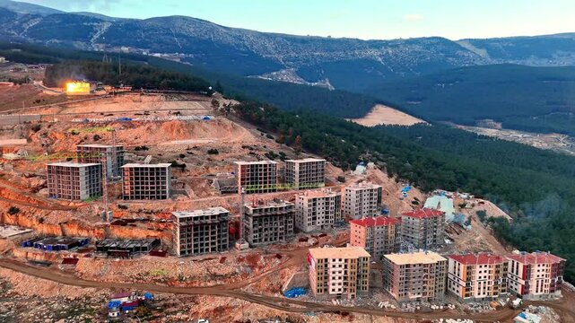 The video shows a multi-story residential construction site. Buildings are at different stages; some in the rough construction phase. The site includes roads, material areas,situated on a hillside.