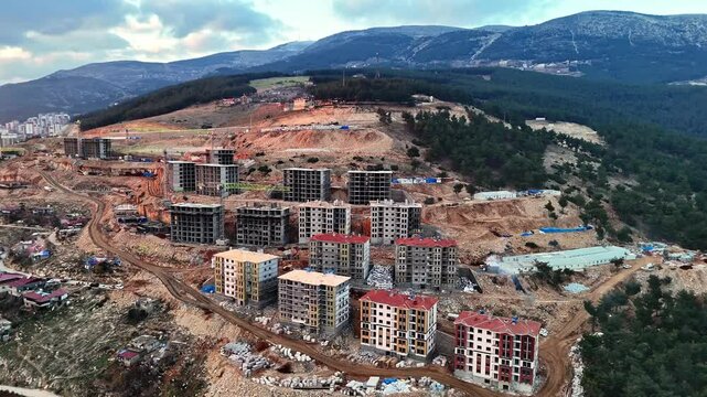 The video shows a multi-story residential construction site. Buildings are at different stages; some in the rough construction phase. The site includes roads, material areas,situated on a hillside.
