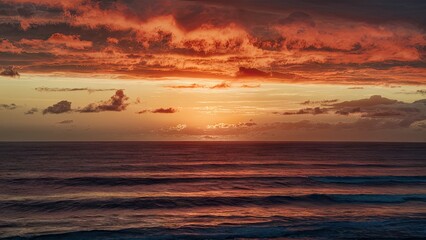 Vibrant sunrise casting warm orange and golden hues over calm ocean waves with light clouds in the sky and gentle ripples in the foreground