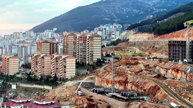 The video shows a multi-story residential construction site. Buildings are at different stages; some in the rough construction phase. The site includes roads, material areas,situated on a hillside.