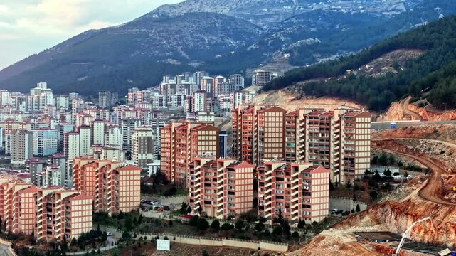 The video shows a multi-story residential construction site. Buildings are at different stages; some in the rough construction phase. The site includes roads, material areas,situated on a hillside.